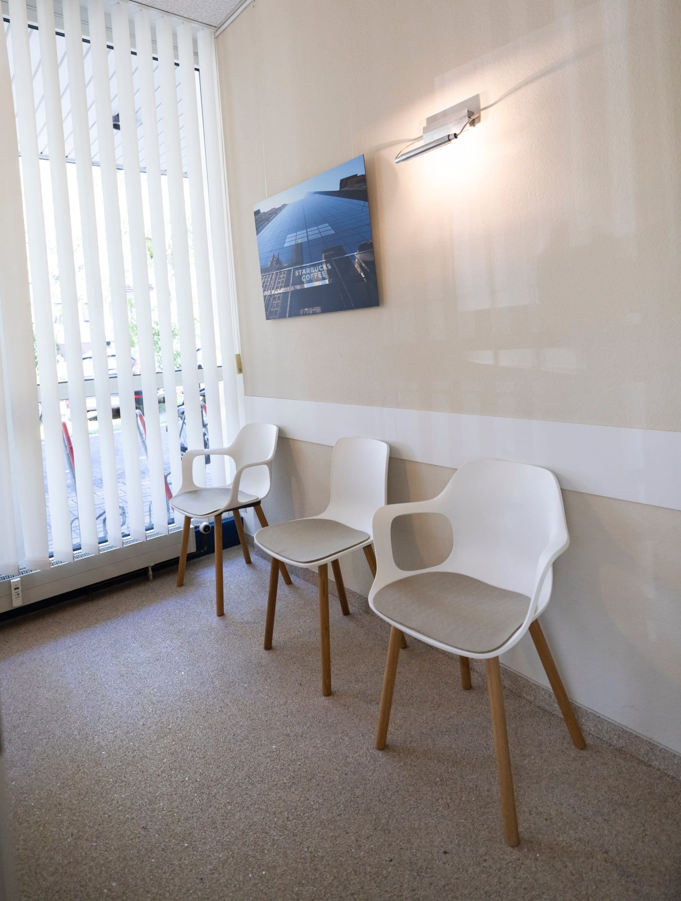 Wartezimmer mit drei weißen Stühle und einem Wandbild